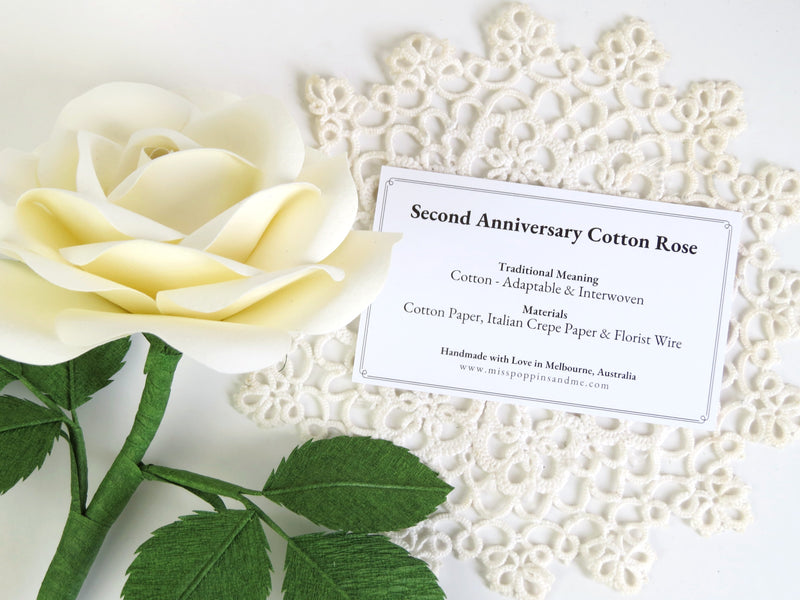 Detail of white cotton paper rose lying on a white doily with product tag