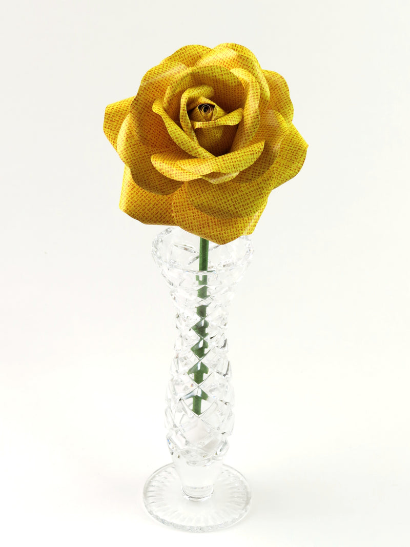 Leafless yellow linen grain paper rose standing in a slender glass vase