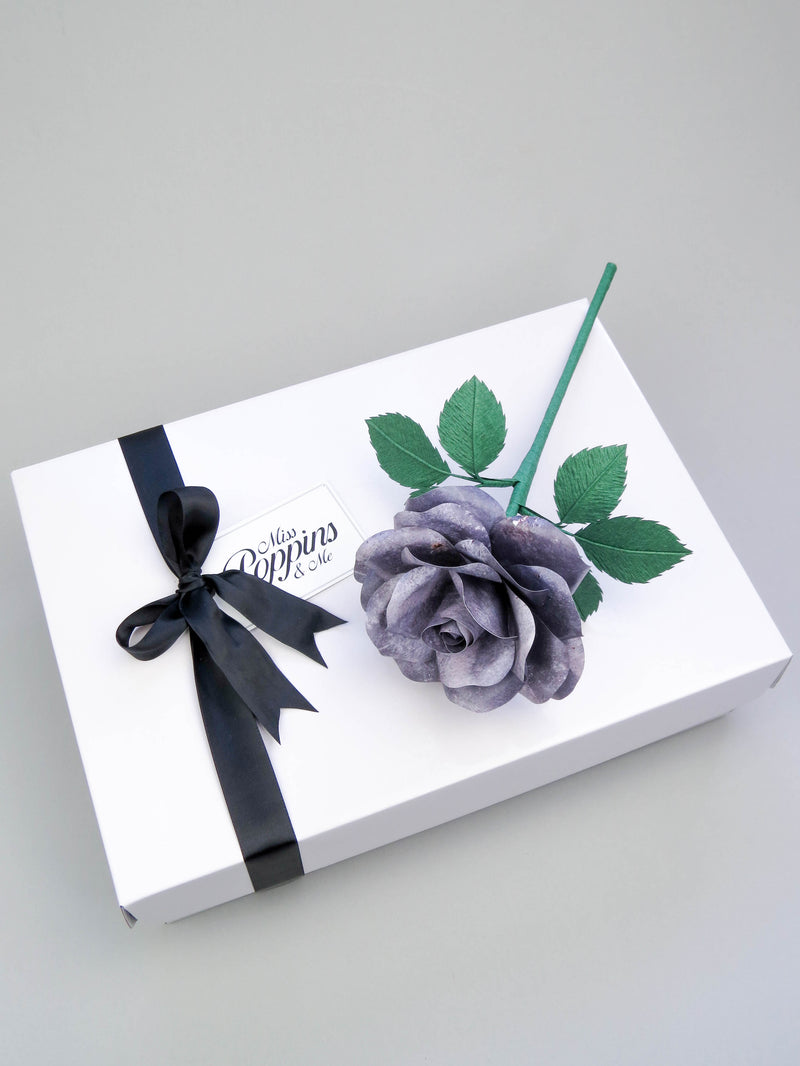 Grey iron paper rose lying on top of a luxury white gift box that has a black satin ribbon tied in a bow with a Miss Poppins and Me gift tag attached