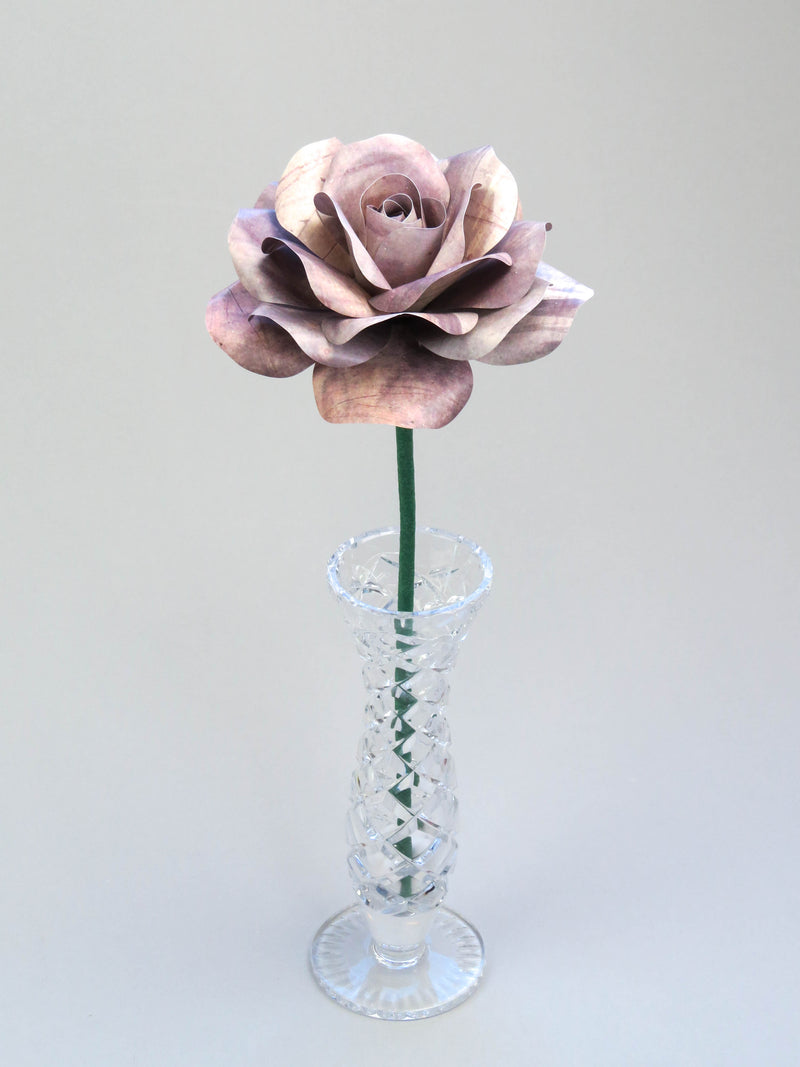 Leafless grey tin paper rose standing in a slender glass vase