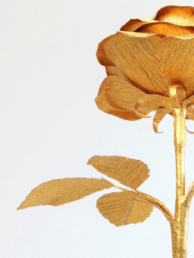 The underneath of the gold crepe paper rose showing the gold calyx with the gold stem and the back of the gold crepe paper leaves