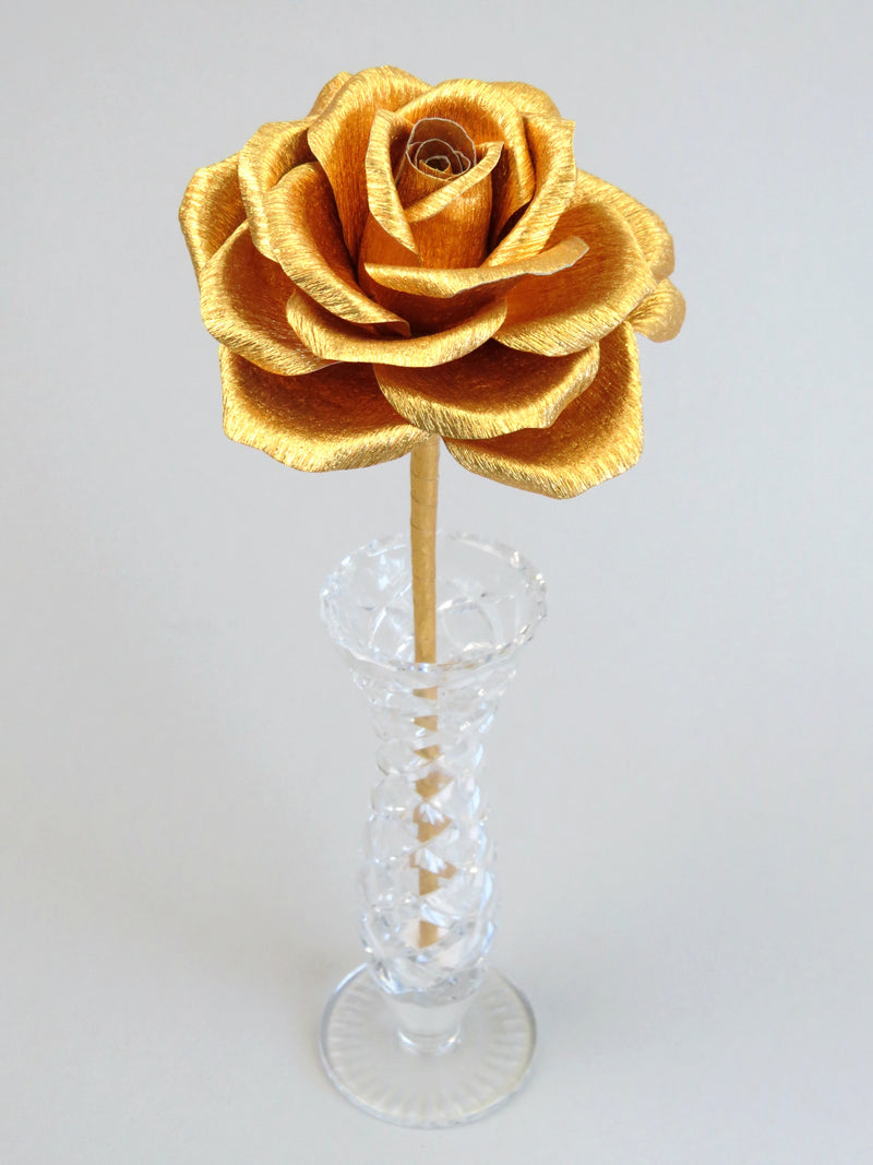 Leafless gold crepe paper rose standing in a slender glass vase