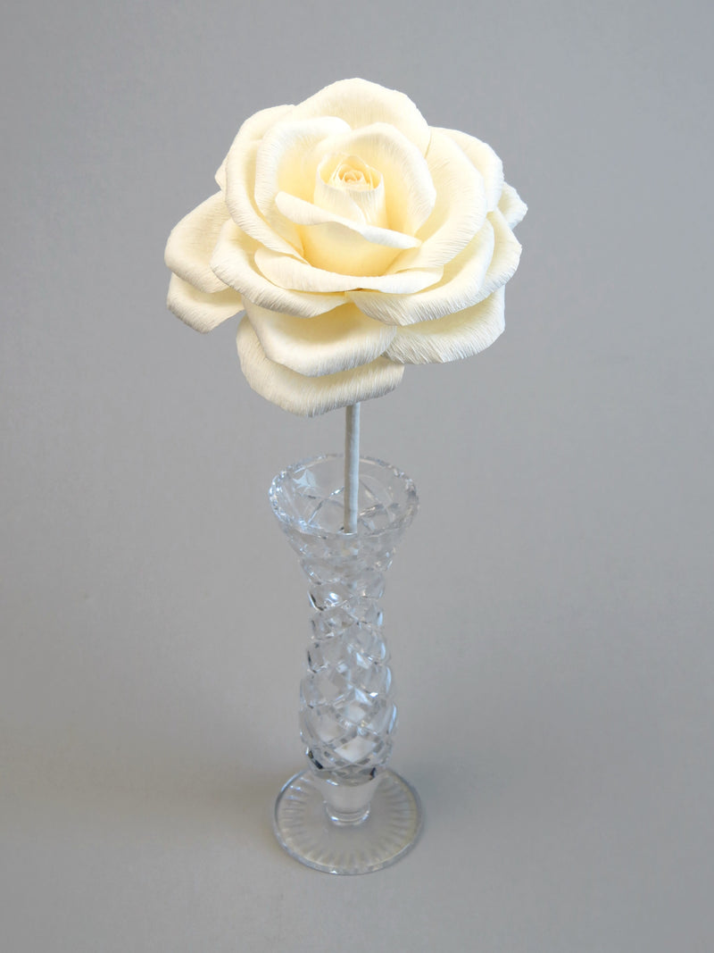 Leafless ivory crepe paper rose standing in a slender glass vase