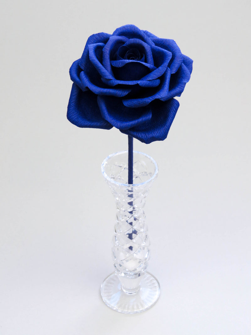 Leafless sapphire blue crepe paper rose standing in a slender glass vase