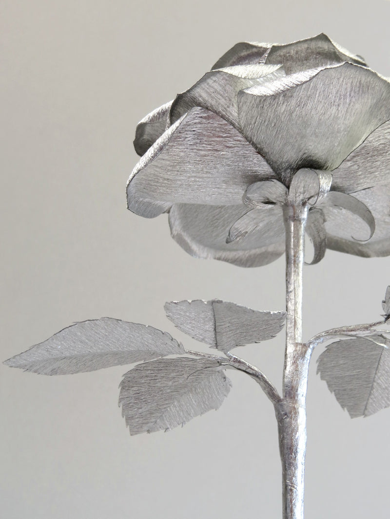 The underneath of the silver crepe paper rose showing the silver calyx with the silver stem and the back of the silver crepe paper leaves