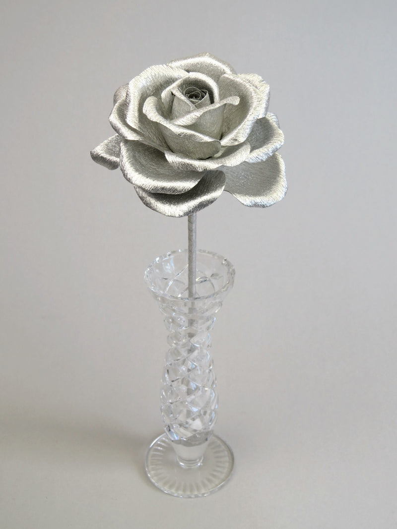 Leafless silver crepe paper rose standing in a slender glass vase