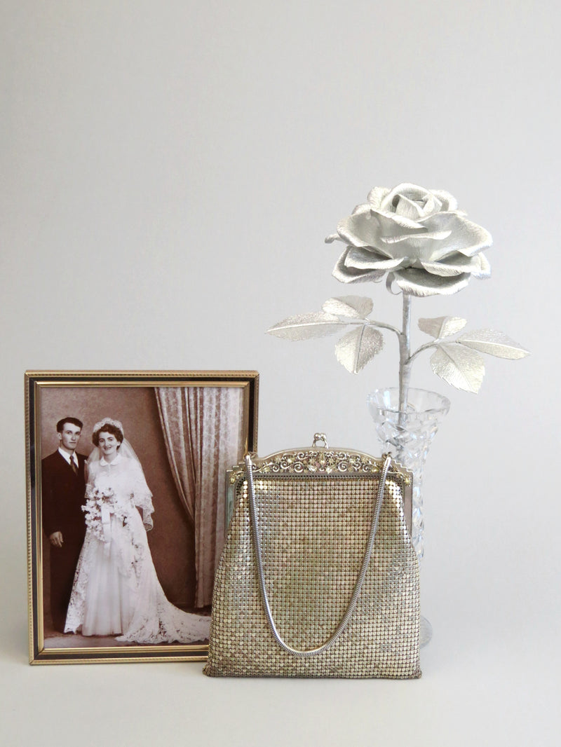 Silver crepe paper rose with six silver leaves standing in a slender glass vase with a thin gold framed sepia wedding photo of a happy vintage bride and groom standing beside it with a vintage silver purse