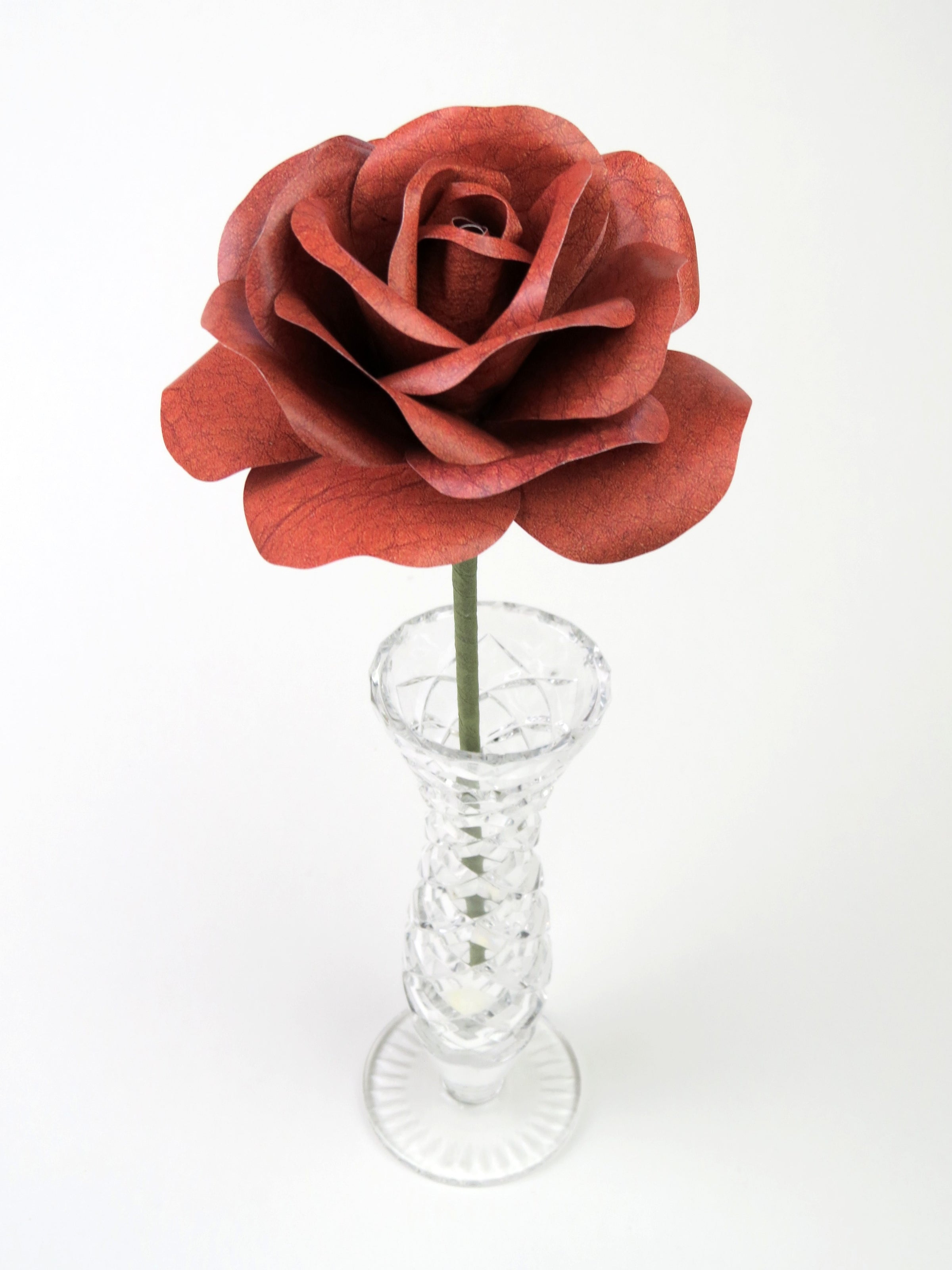 Leafless brown leather grain paper rose standing in a slender glass vase