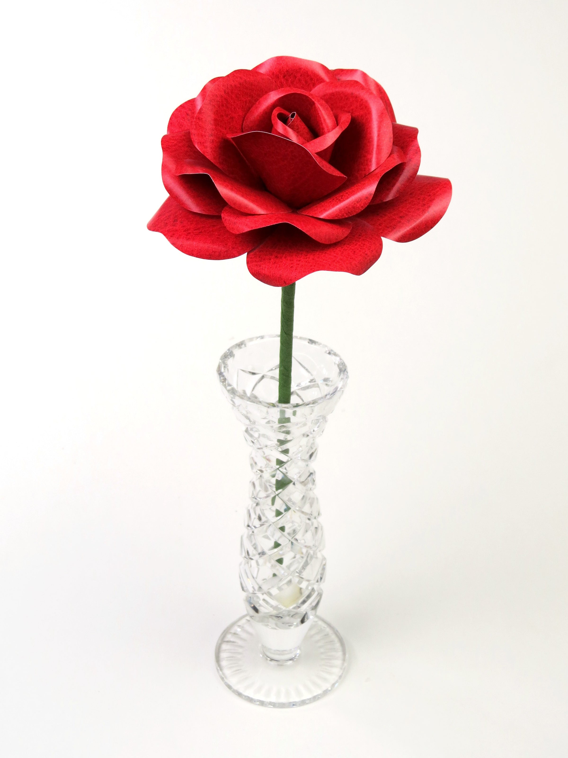 Leafless red leather grain paper rose standing in a slender glass vase