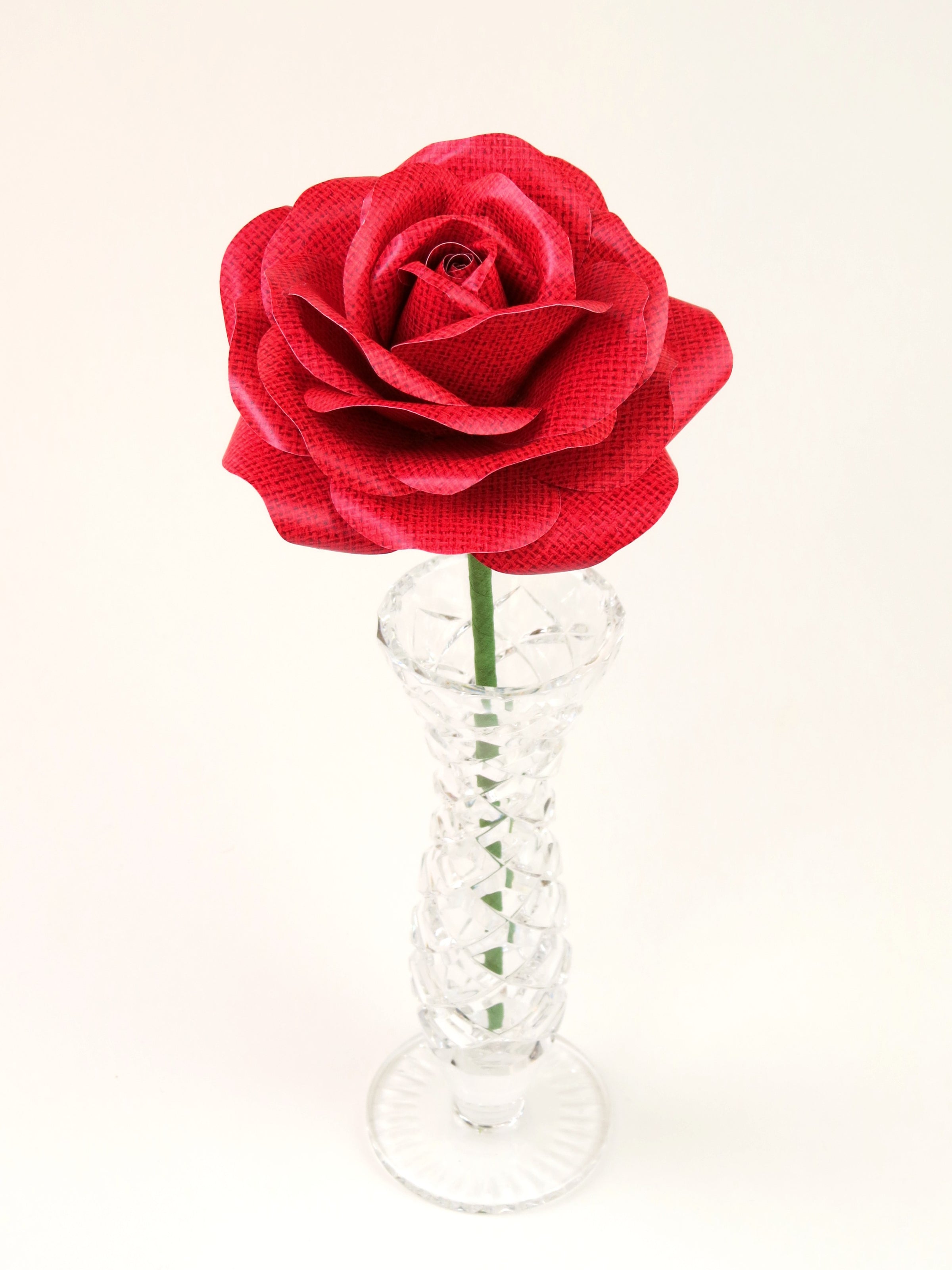 Leafless red linen grain paper rose standing in a slender glass vase