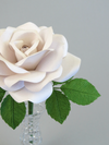 Close up detail of the texture on the petals of a white linen grain paper rose, with ivy green leaves, and the hint of the top of the glass vase