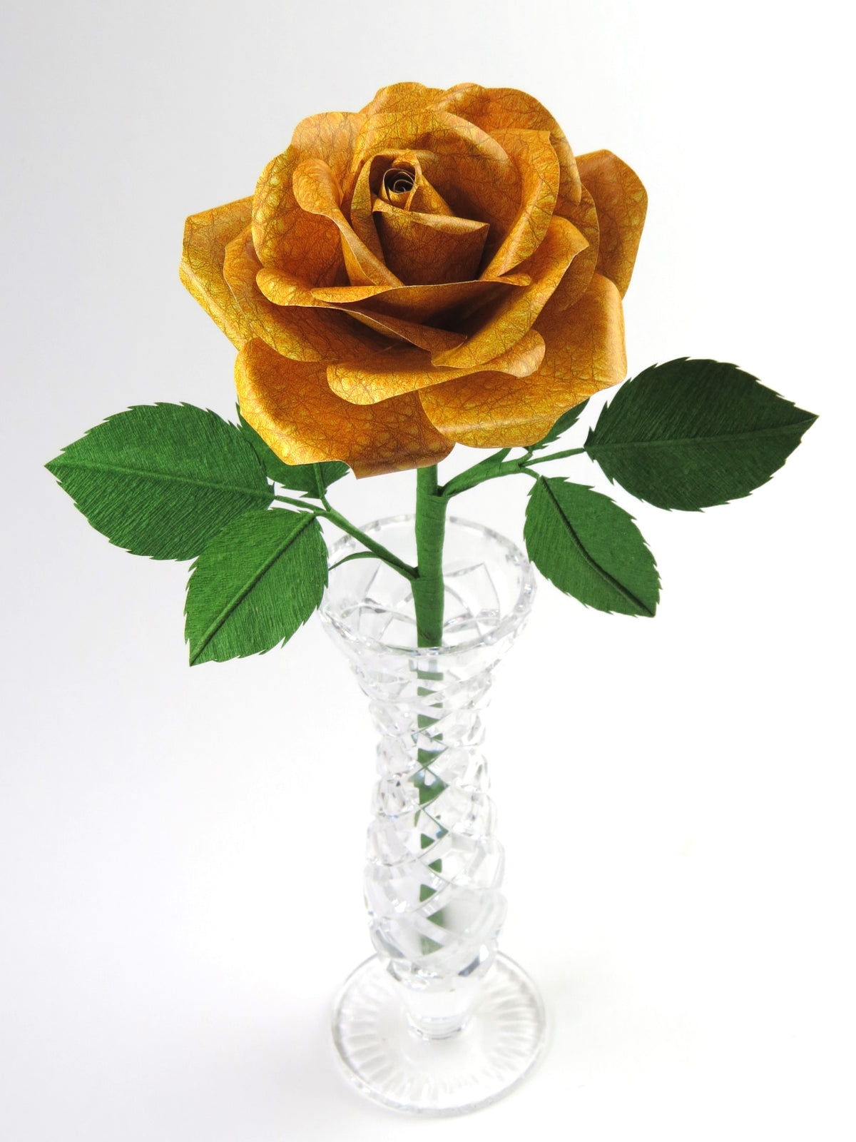 Yellow grain leather paper rose with six leaves standing in a narrow glass vase against a white background