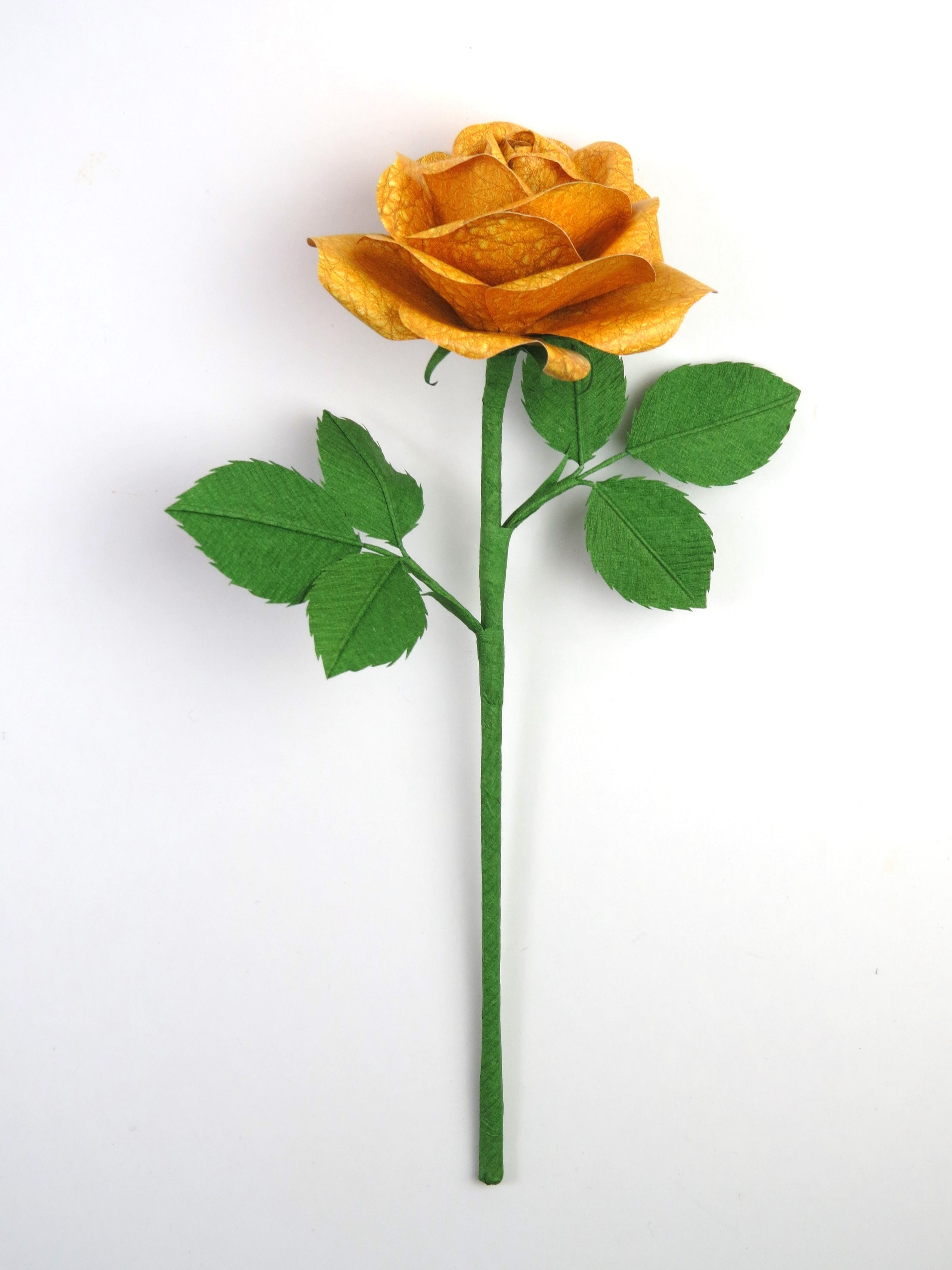 Bright yellow leather grain paper rose lying in a vertical position with 6 ivy green crepe paper leaves