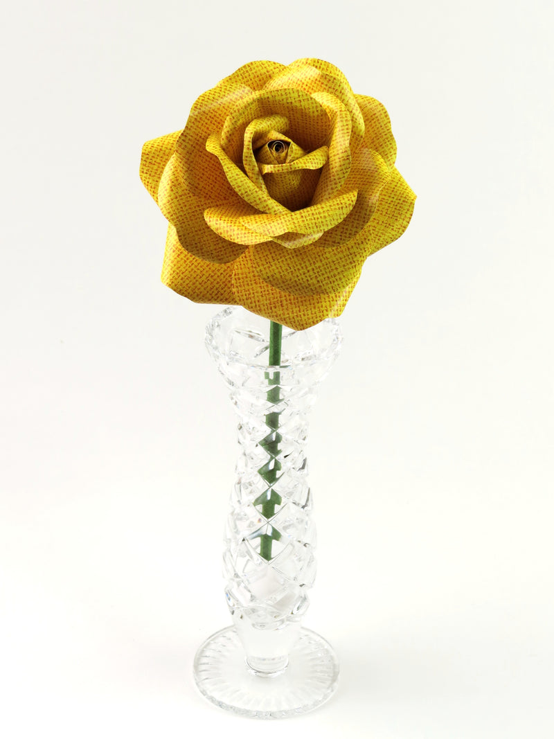 Leafless yellow linen grain paper rose standing in a slender glass vase